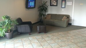 A lobby with a grey couch, a black armchair, a potted plant, and a flat-screen TV mounted on the wall. - Shemron Suites Hotel (Deep River)