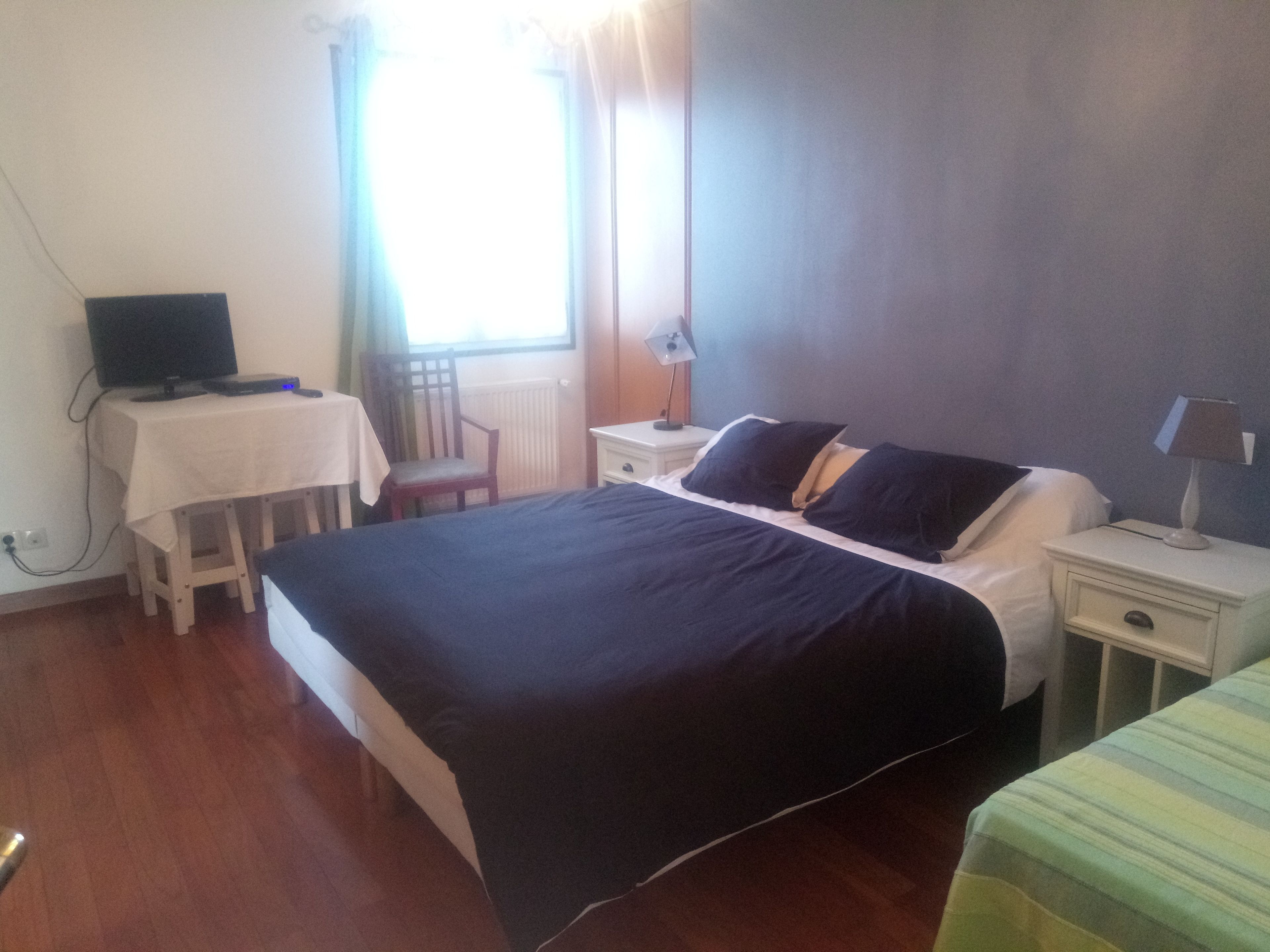Een slaapkamer met een bed, bureau, stoel, televisie en raam.