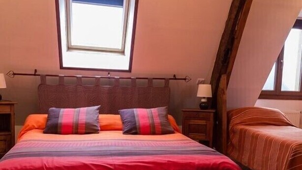 A bedroom with a large bed, two pillows, a nightstand, a lamp, and a window. - La Ferme de Bout de la Ville (Criquebeuf-en-Caux)