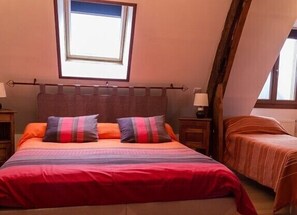 Un dormitorio con una cama grande, dos almohadas, una mesita de noche, una lámpara y una ventana.