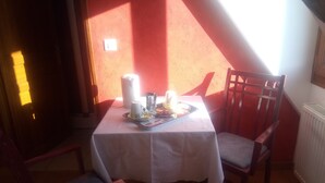 A dining area with a table set for two, a chair, and a window with sunlight casting shadows. - La Ferme de Bout de la Ville (Criquebeuf-en-Caux)