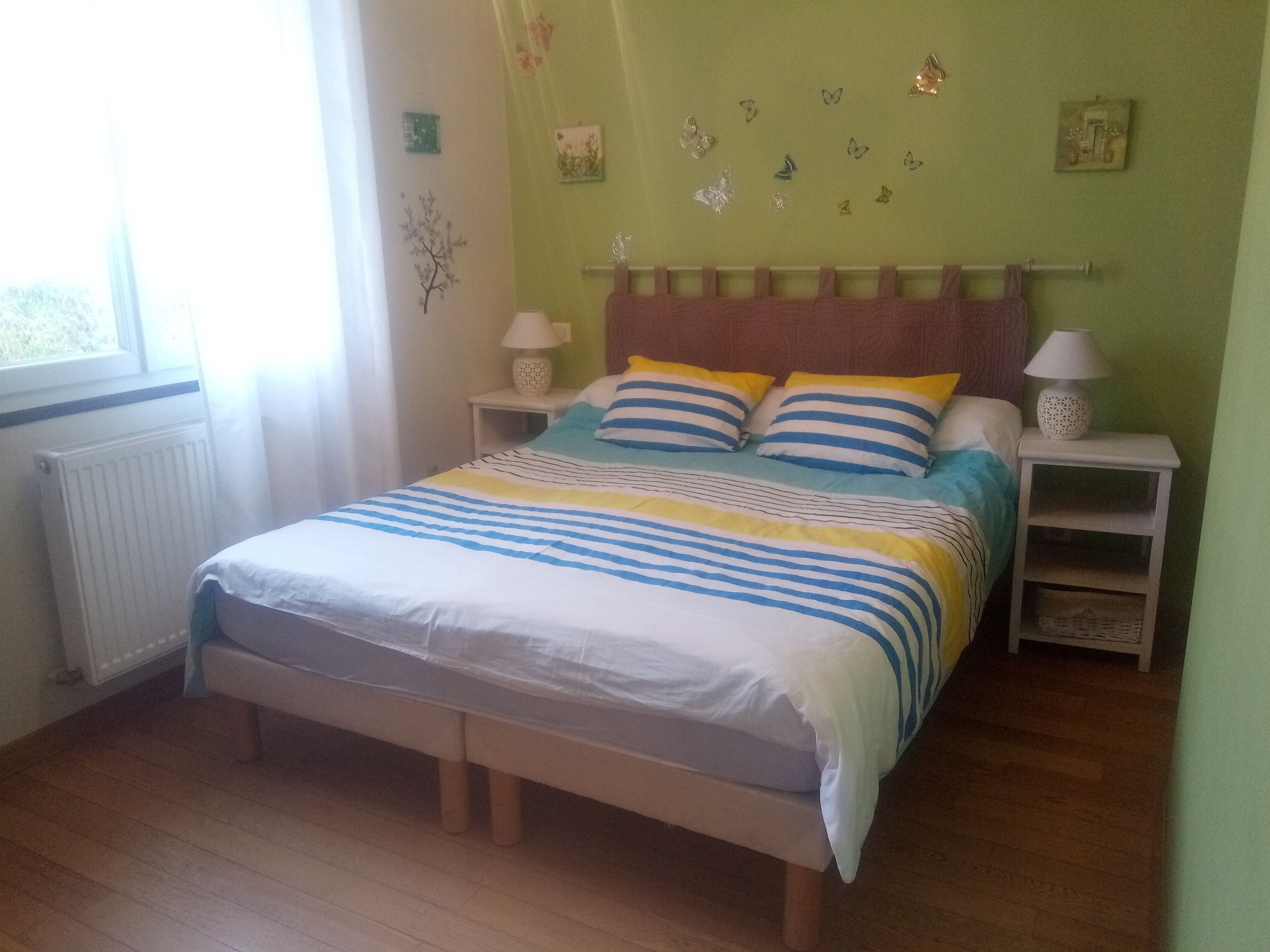A bedroom with a bed, two bedside tables, a window, and a radiator.