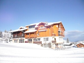 A multi-story wooden building with balconies, surrounded by snow-covered landscape. - Hôtel les skieurs (Bellevaux)