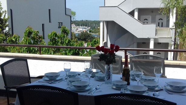 A dining table set with white plates, bowls, and cutlery, with a vase of red roses and a bottle of champagne. - Ida Pjescana (Medulin)