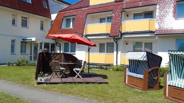 Ein Wohngebäude mit Balkon, einer kleinen Sitzgelegenheit mit Tisch und Stühlen sowie einem roten Sonnenschirm.
