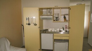 Eine kleine Küchenzeile mit Herd, Spüle und kleinem Kühlschrank, sowie ein Set an Geschirr, das an der Wand hängt.