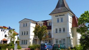 Ein mehrgeschossiges Gebäude namens Villa Viktoria mit einem markanten Turm, umgeben von Grünflächen und parkenden Autos.