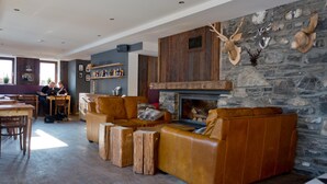 A cozy living area with a stone fireplace, leather sofas, and wooden accents. - Hideout Hostel (Morzine)
