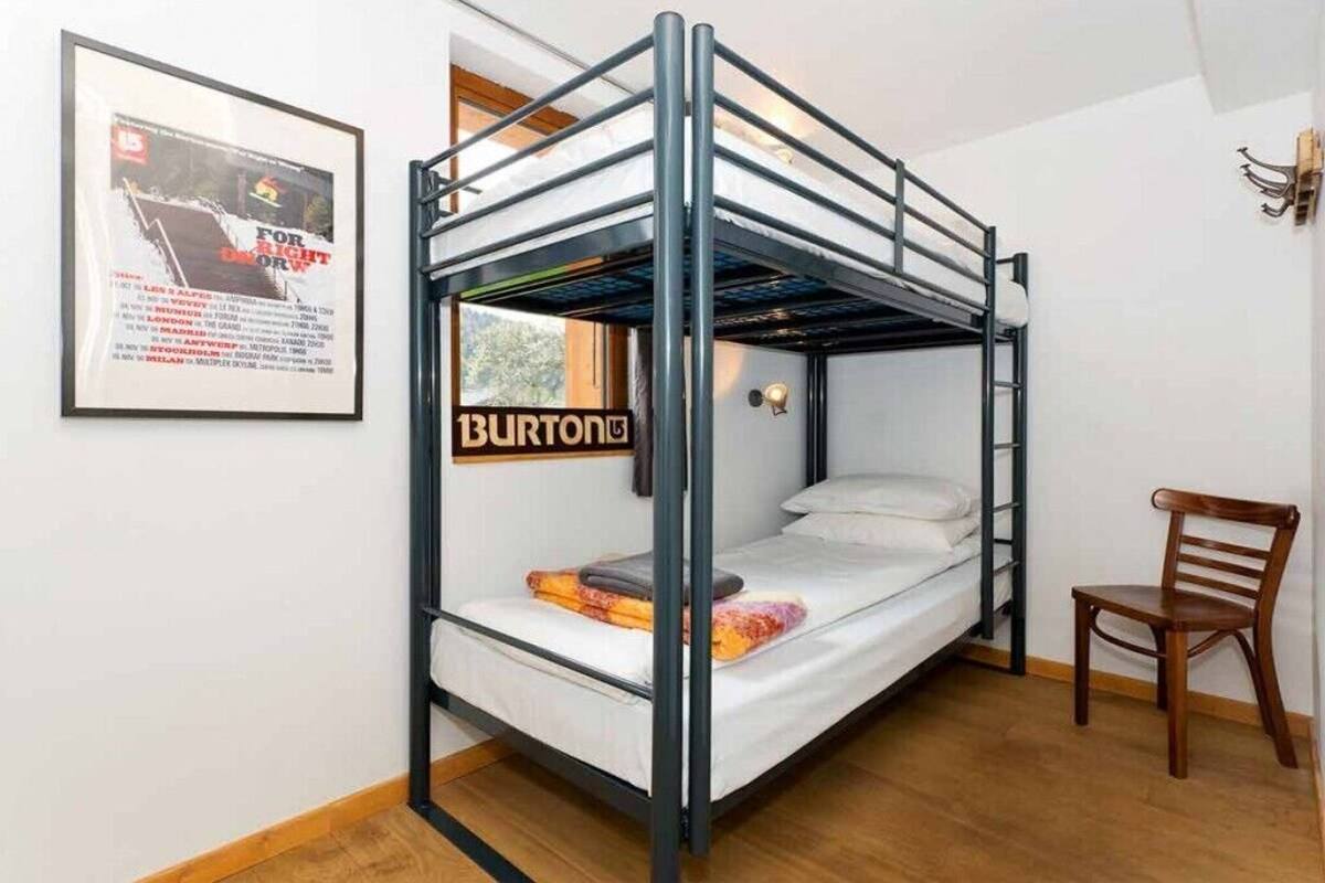 A bunk bed with a black metal frame, a white mattress, and a wooden chair.