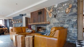 A cozy living room with a stone fireplace, leather sofas, and wooden stools. - Hideout Hostel (Morzine)