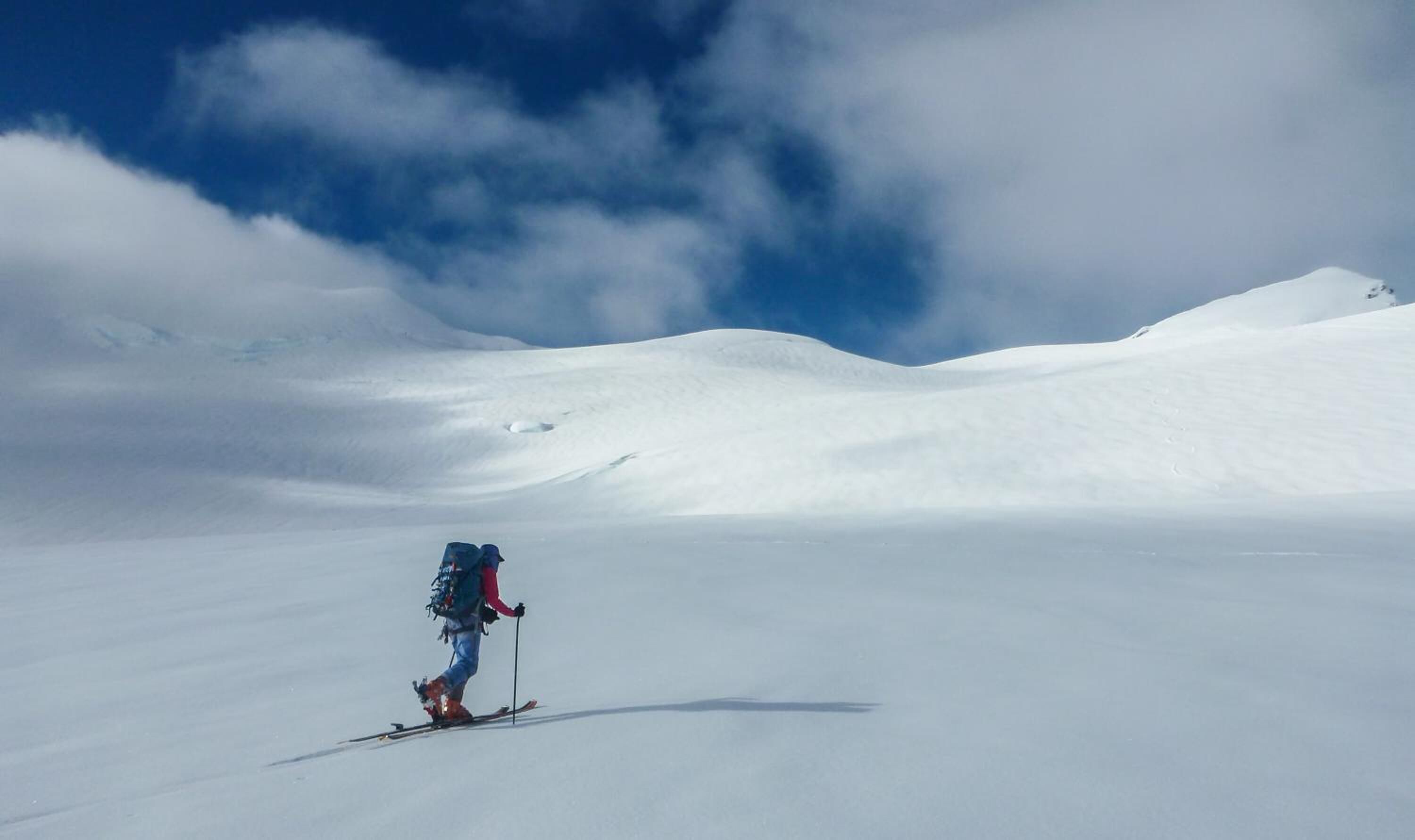 Una persona esquiando en una pendiente cubierta de nieve, con cielo despejado y nubes al fondo.