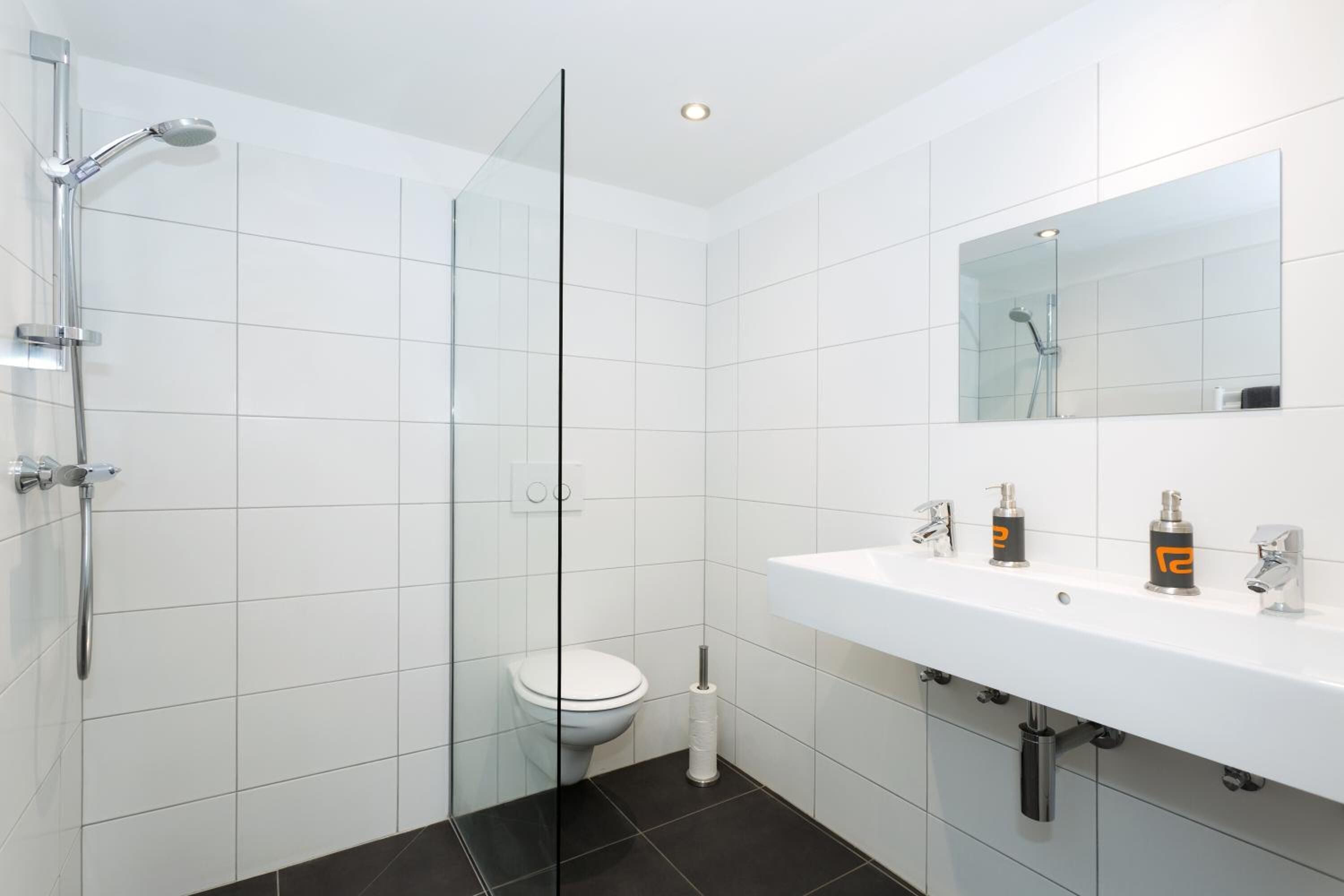 Ein modernes Badezimmer mit Duschkabine aus Glas, einem weißen Waschbecken mit zwei Seifenspendern und einer Toilette.