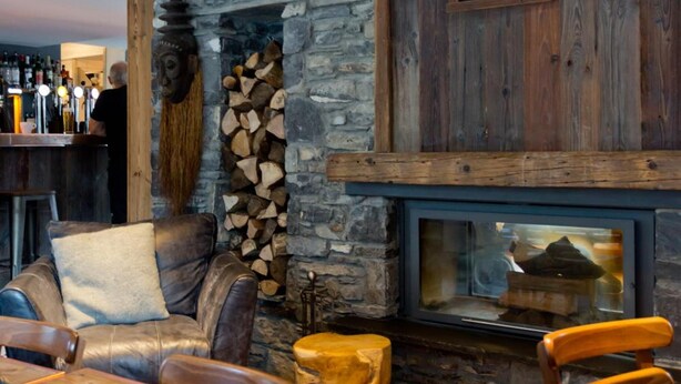 A rustic interior with a stone fireplace, wooden walls, and a bar area. - Hideout Hostel (Morzine)