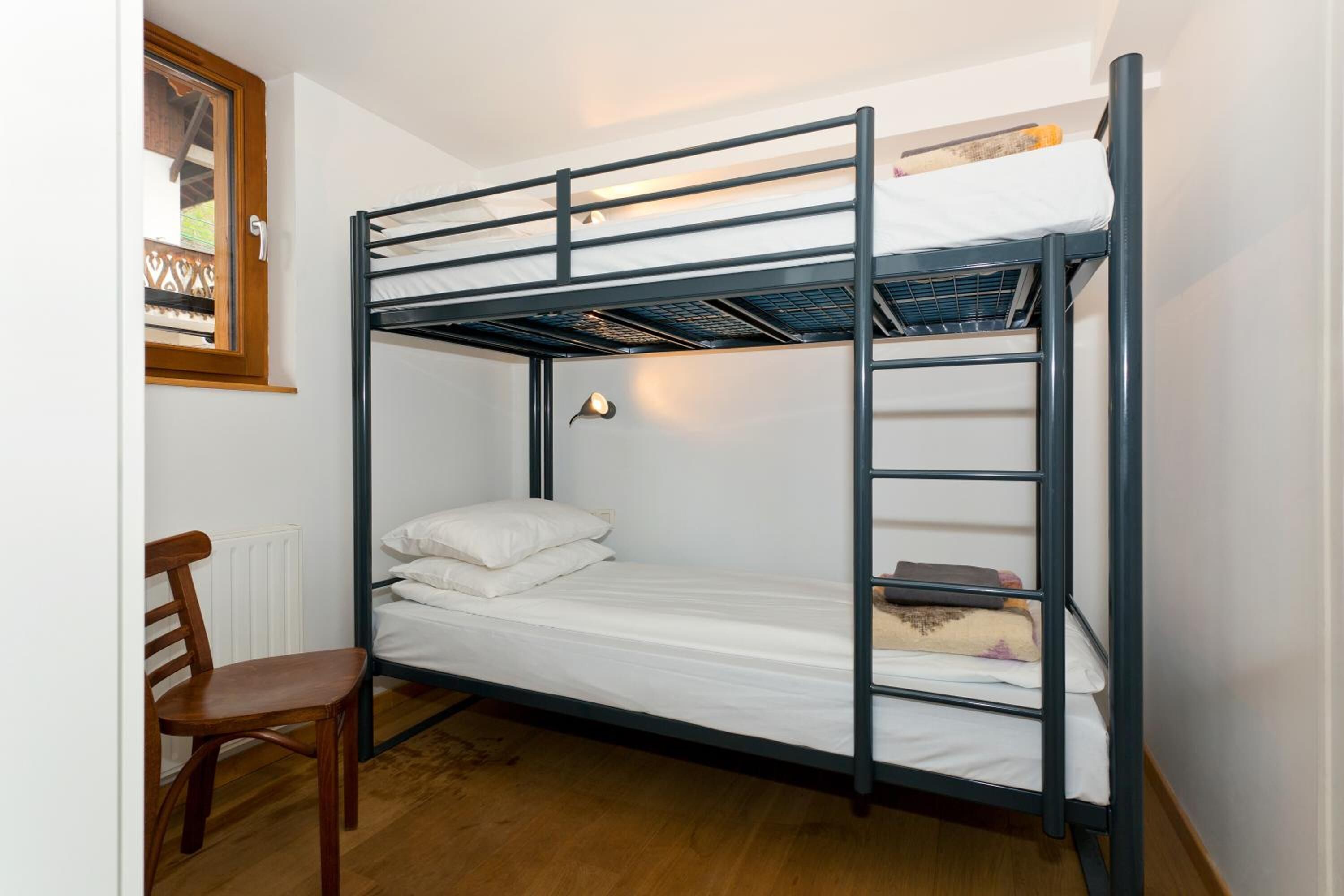 Een stapelbed met een houten stoel, een klein tafeltje en een raam met uitzicht op de omgeving.