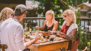 A group of people dining outdoors at a wooden table with various dishes and drinks. - Hideout Hostel (Morzine)