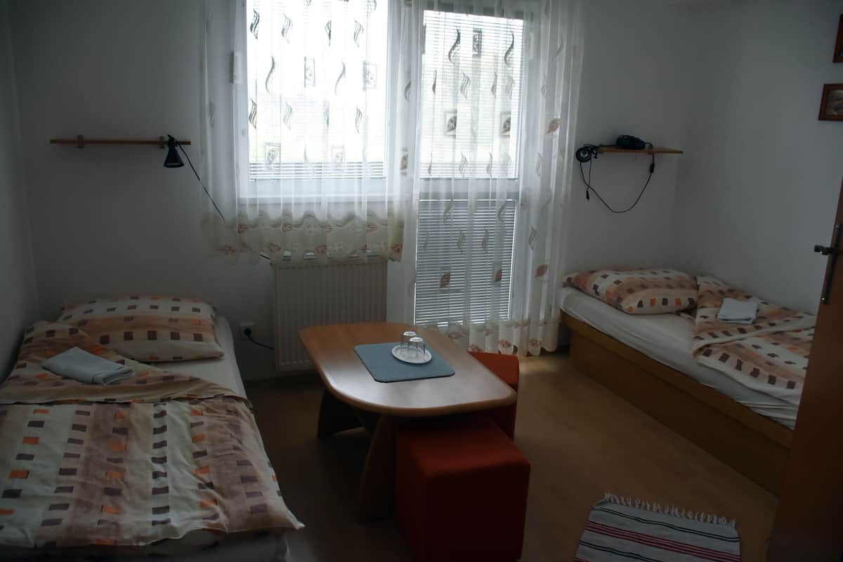 A small, well-lit room with two beds, a table, and a bench.