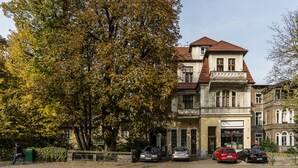 Een gebouw met twee verdiepingen in traditionele architectuur, met een balkon op de bovenverdieping en een inkom op de begane grond.
