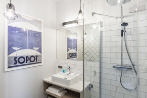 Een moderne badkamer met een wit wastafelmeubel, spiegel en douche. Er hangt een lijst aan de muur en een handdoekrek onder het wastafelmeubel.