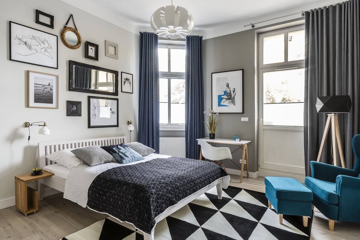 A bedroom with a bed, bedside table, lamp, chair, and artwork on the wall.