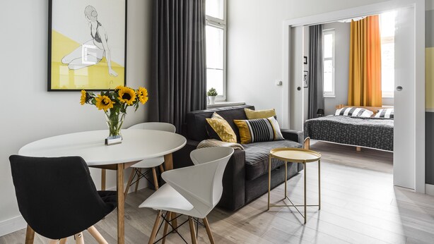Een moderne woonkamer met een zwarte bank, witte stoelen, een klein rond tafeltje en een kunstwerk in een lijst aan de muur.