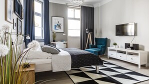 Een moderne slaapkamer met een bed, bureau, stoel, televisie en een groot raam met gordijnen.