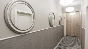 Een hal met drie ronde spiegels aan de muur, een houten deur aan het einde, en een vloer met een patroon.