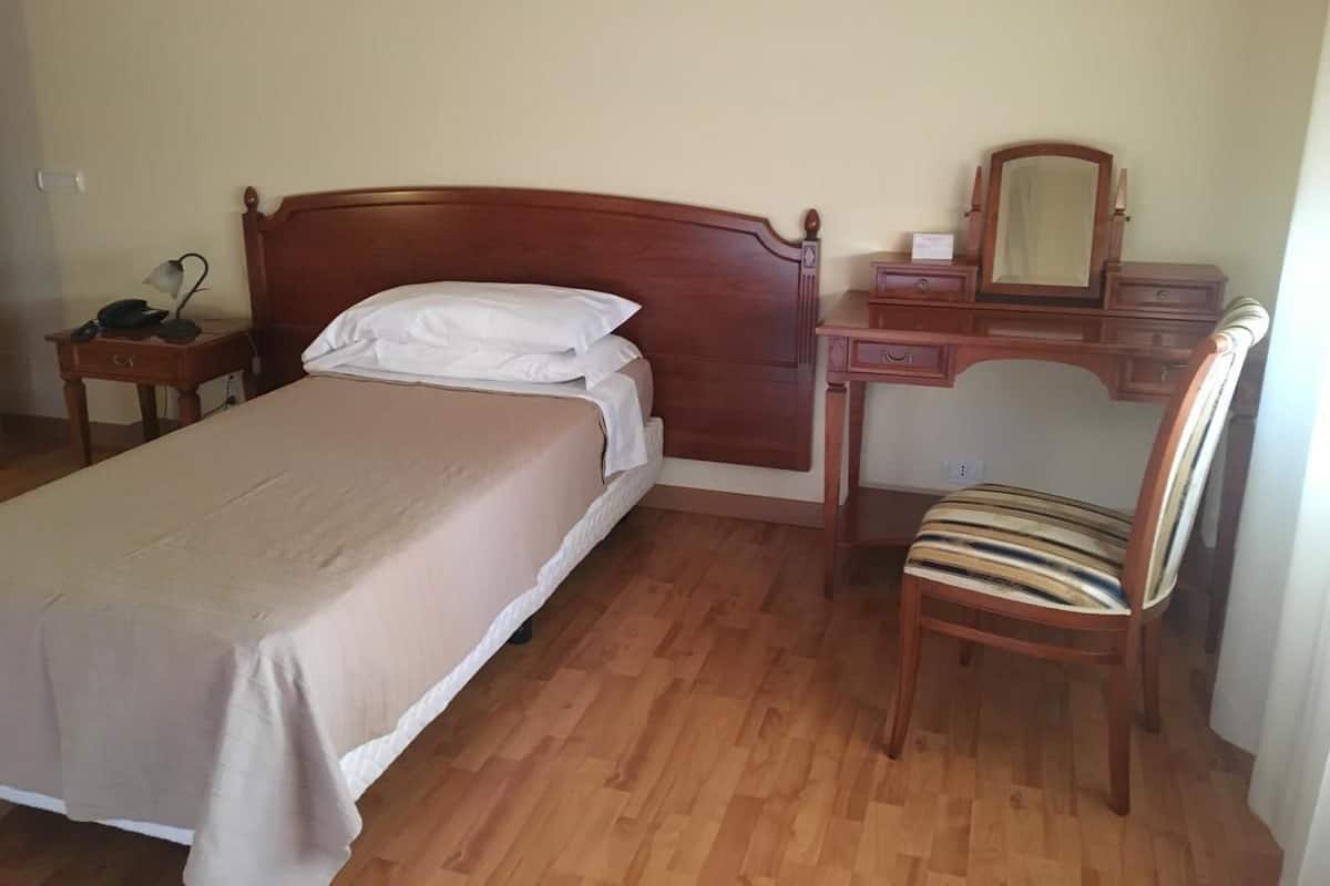 A bedroom with a wooden bed, a desk with a mirror, and a striped chair.