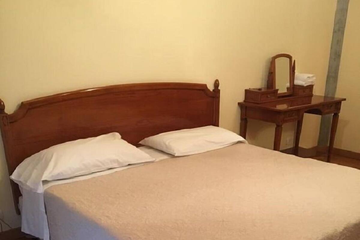A single-bed room with a wooden headboard, a bedside table with a mirror, and a wooden nightstand.