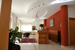 Amplia sala de estar con un mostrador de recepción de madera, una pared de acento roja y una planta grande.