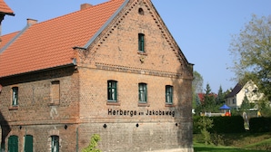 A brick building with a red-tiled roof and green shutters, labeled "Herberge am Jakobsweg". - Herberge am Jakobsweg (Weissenfels)