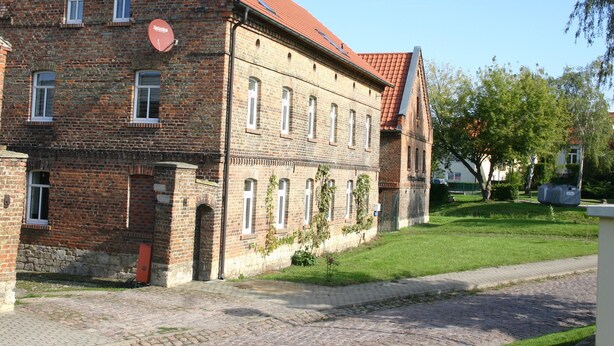 A historic brick building with a red-tiled roof, multiple windows, and a small garden area. - Herberge am Jakobsweg (Weissenfels)