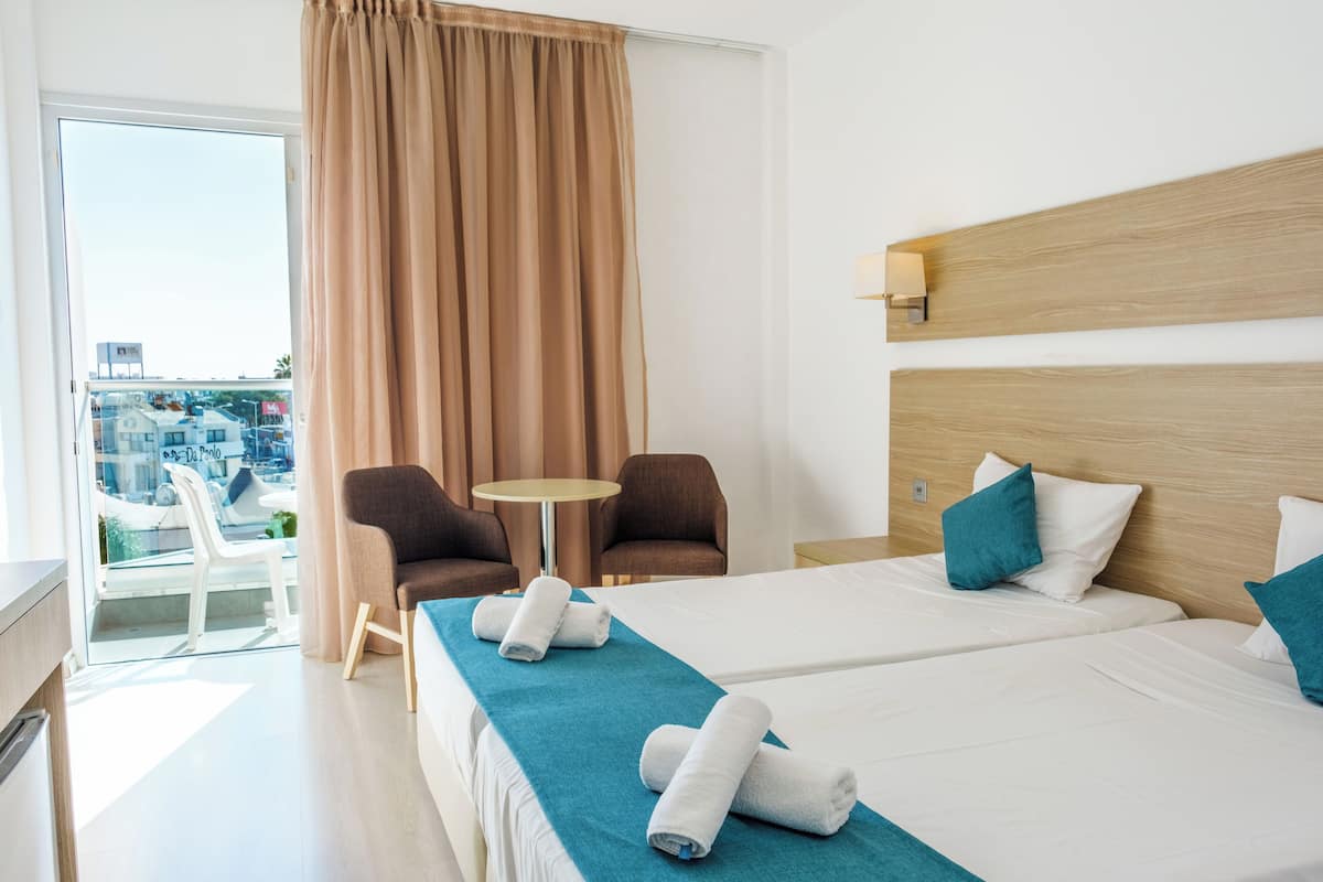 A hotel room with two beds, a balcony, and a view of the city.