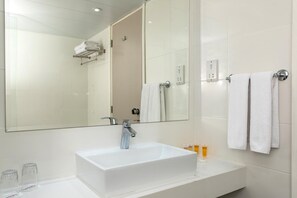 A modern bathroom with a large mirror, a white sink, and two towels hanging on the wall. - Kapetanios Bay Hotel Protaras (Paralimni)