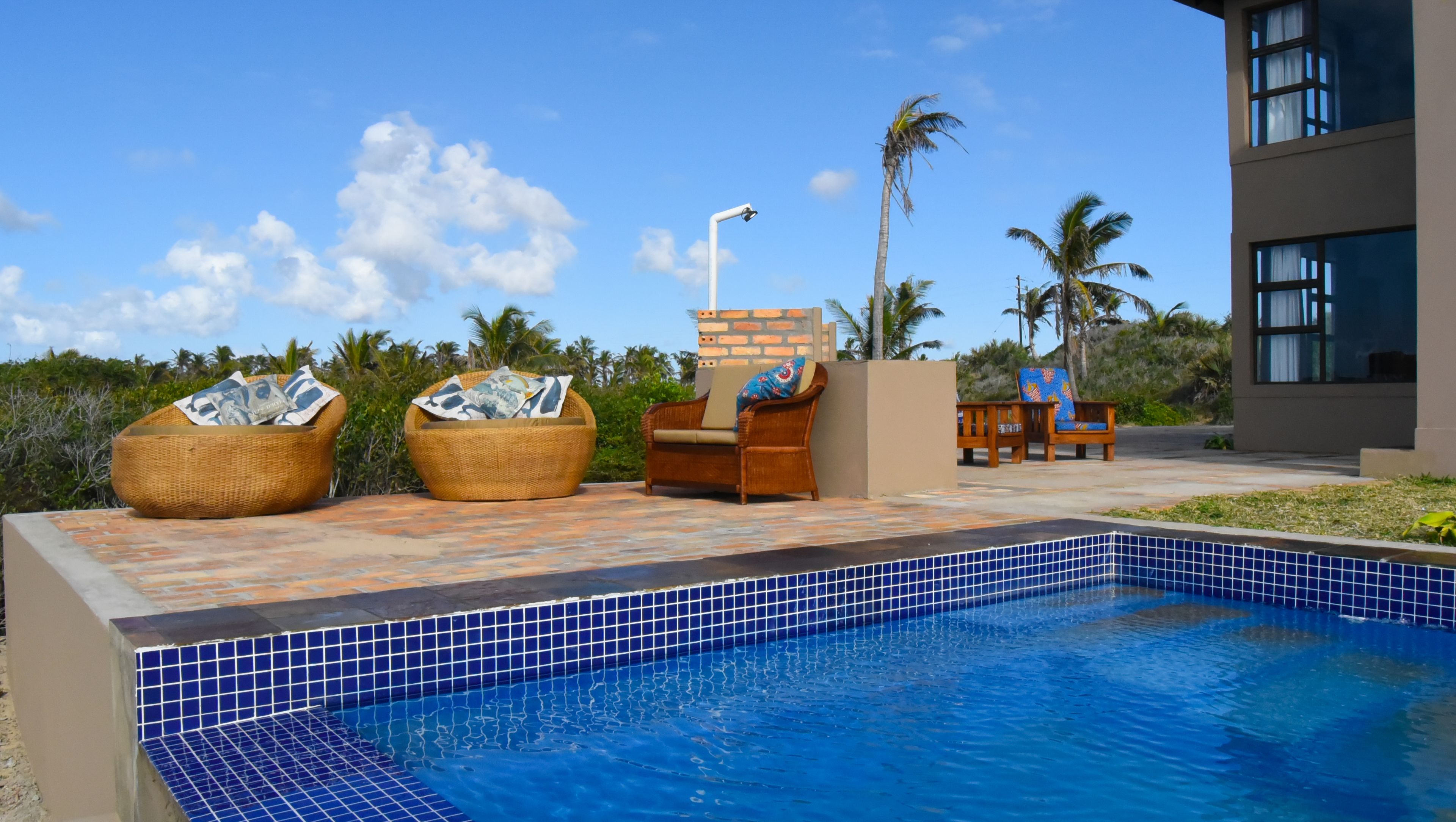 A pool area with wicker chairs, a lounge chair, and a small pool with blue tiles.