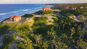 A coastal resort with multiple buildings, sandy paths, and lush greenery. - Villa Castellos (Jangamo)