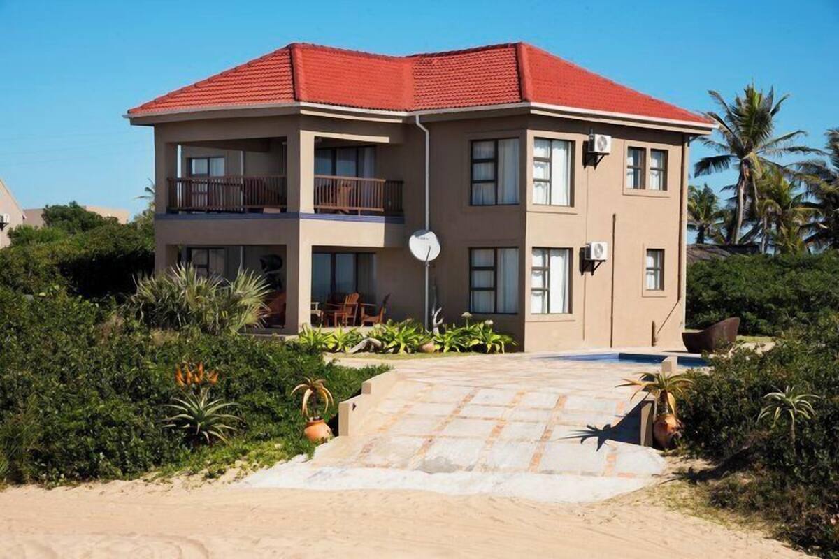 A two-story building with a red roof, a balcony on the upper floor, and a paved entrance.