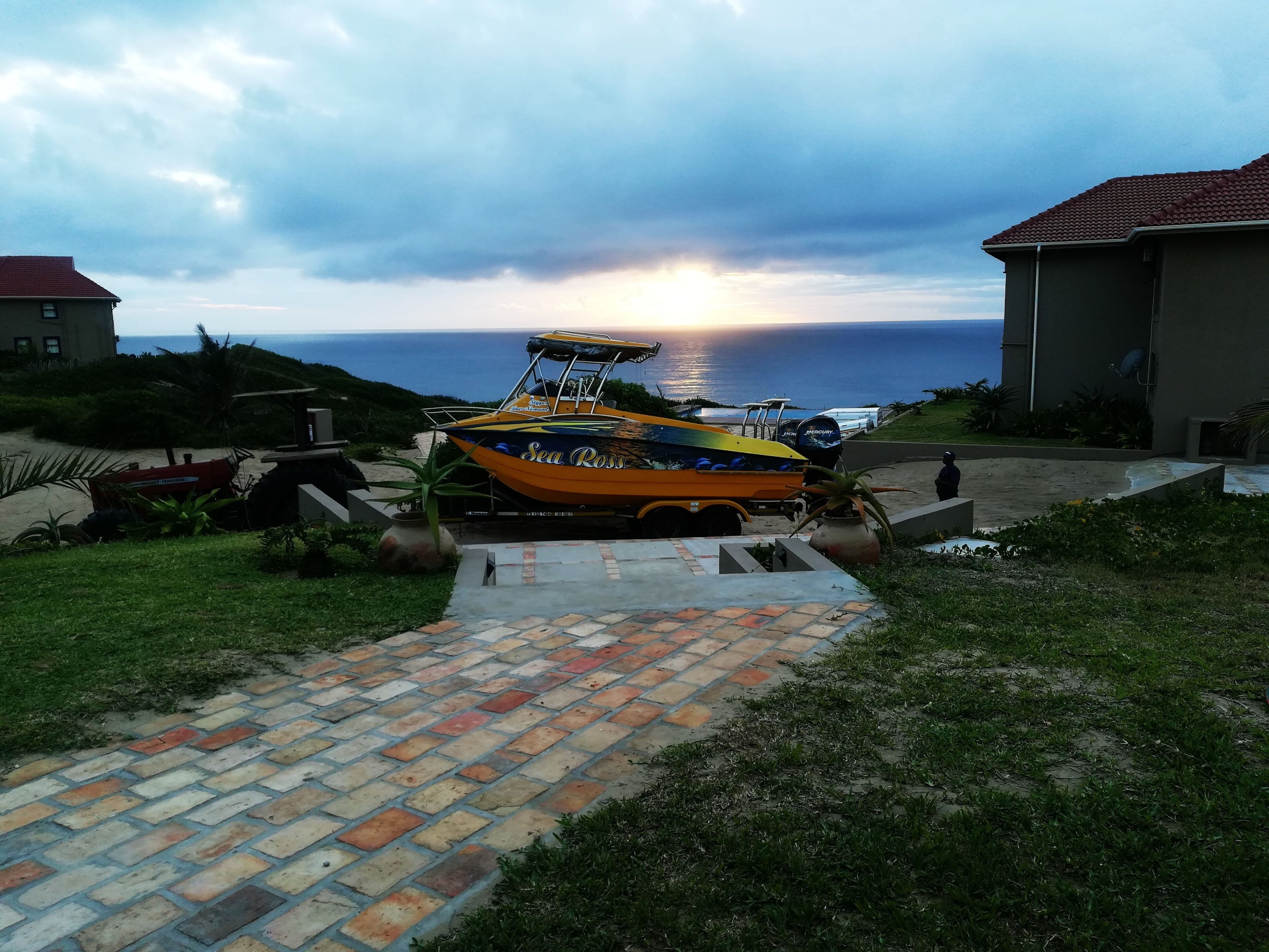Un bateau est garé sur un chemin pavé, offrant une vue sur l’océan, avec un bâtiment en arrière-plan.