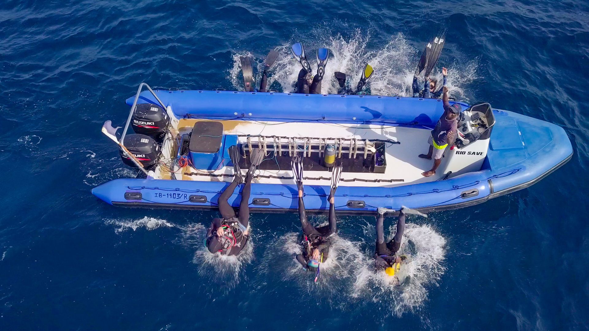 Un bote inflable azul con un motor fueraborda Suzuki, equipado con remos y chalecos salvavidas.
