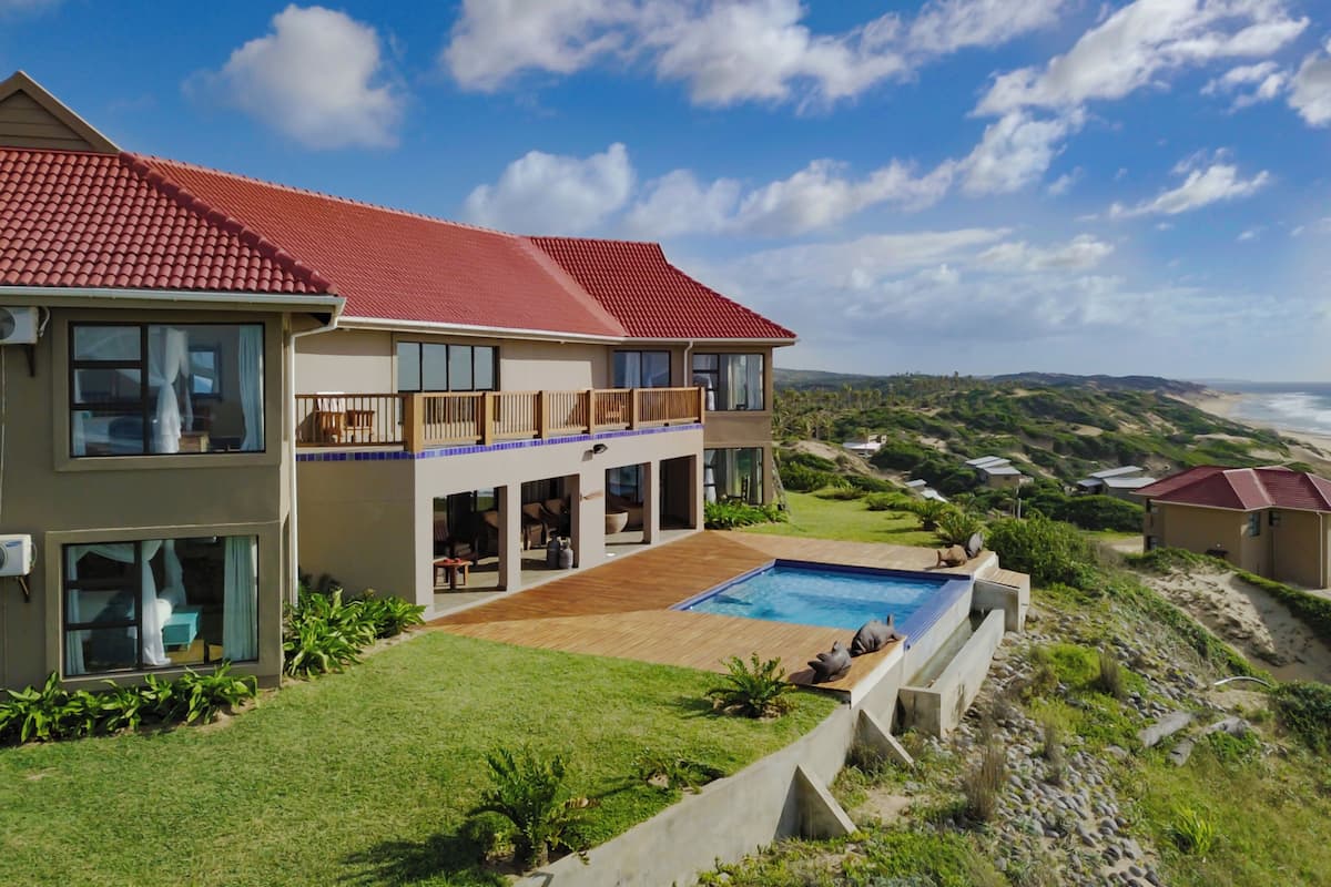 A two-story house with a red-tiled roof, large windows, and a swimming pool.