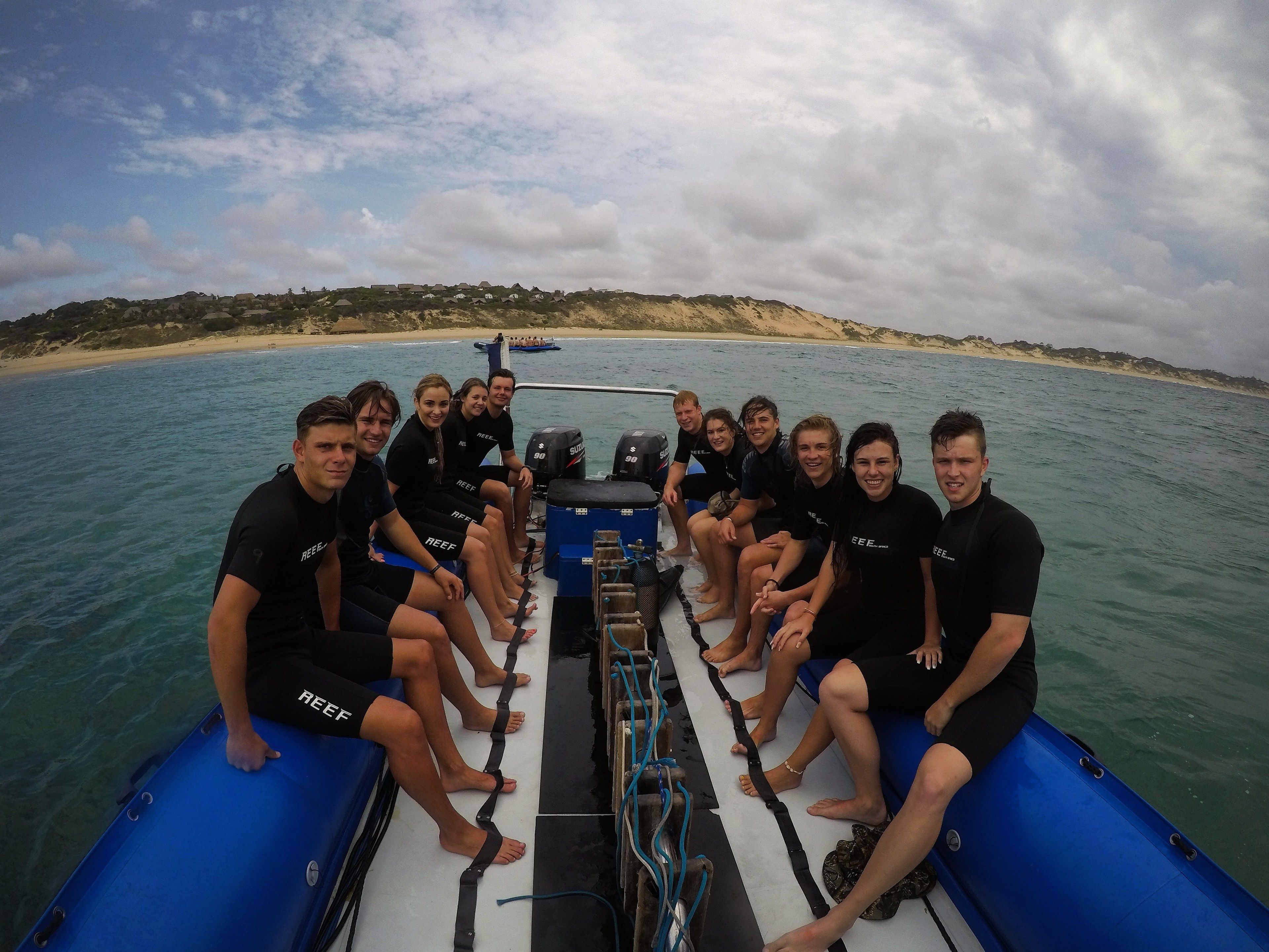A group of people on a boat with a sandy beach and hills in the background.