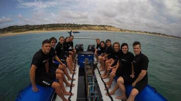 A group of people on a boat with a sandy beach and hills in the background.