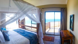 A bedroom with a large bed, a wooden headboard, a nightstand, and a view of the ocean through a balcony door. - Villa Castellos (Jangamo)