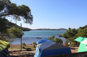A campsite with tents and a view of a calm lake with boats. - Camlik Kamping (Ayvalik)