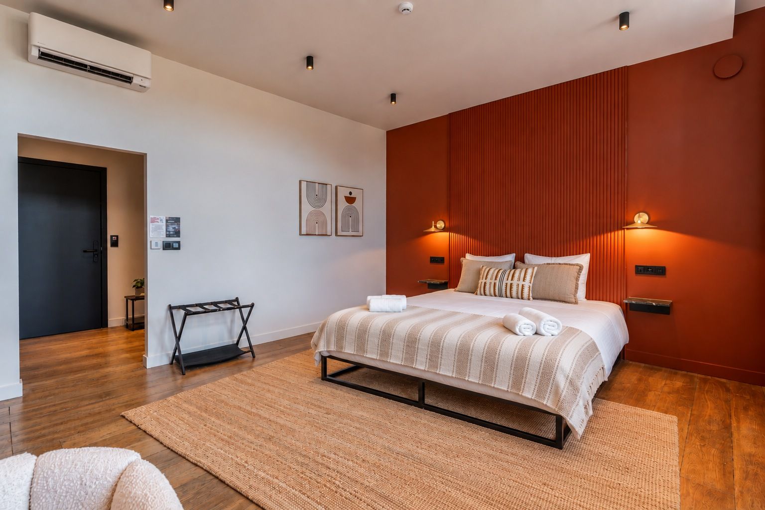 Una habitación de hotel moderna con cama, mesitas de noche, aire acondicionado instalado en la pared y una puerta que da a otra habitación.