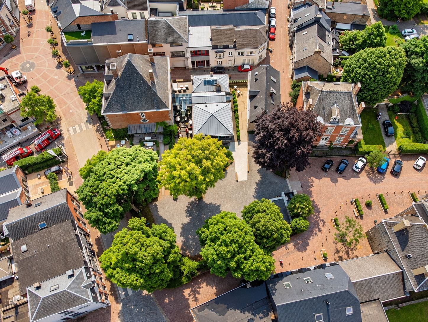 An aerial view of a residential area with a central building surrounded by trees and parked cars.