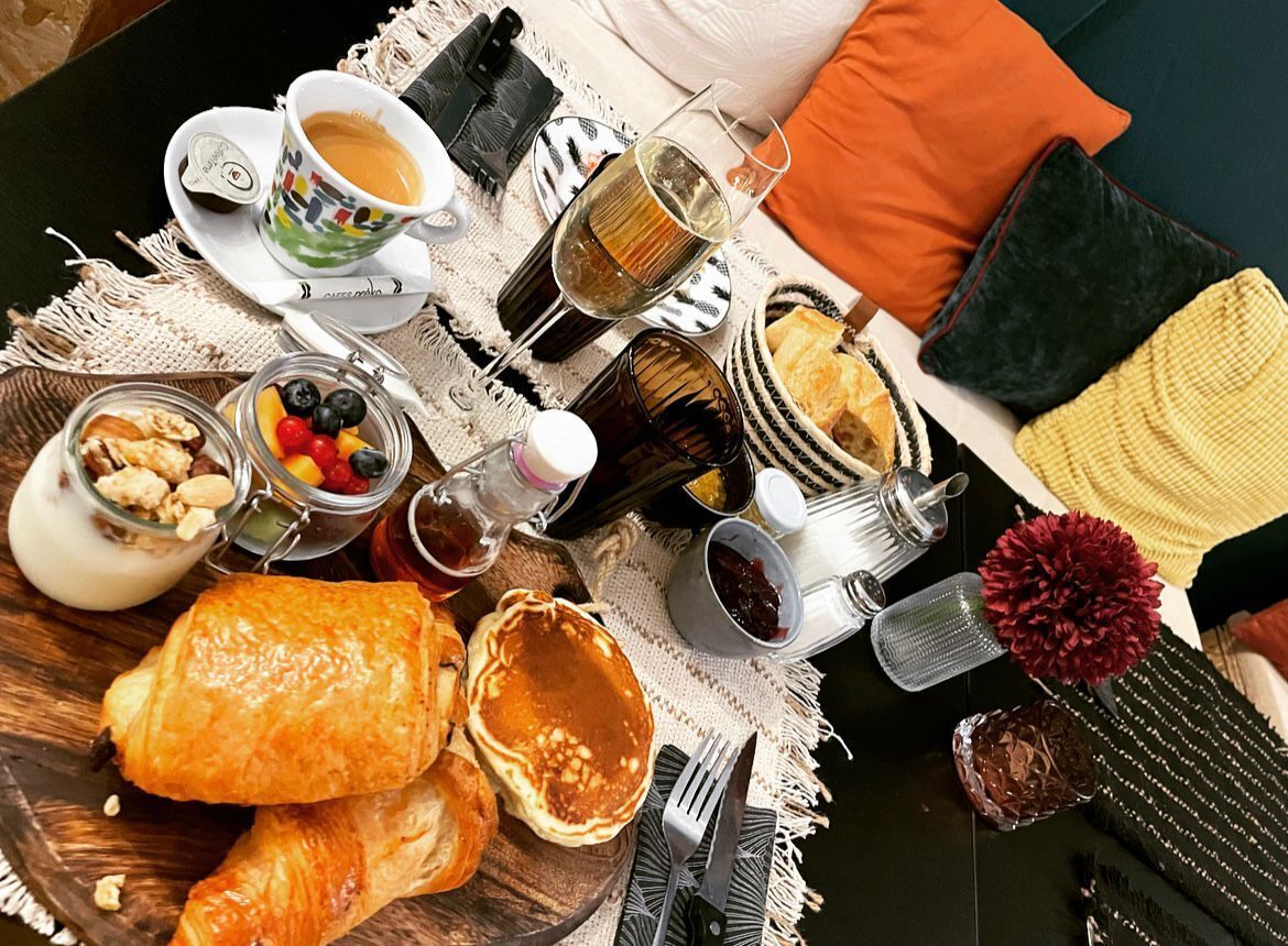 Ein Frühstückstisch mit Croissants, Gebäck, einer Kaffeetasse, einem Weinglas und verschiedenen Gewürzen.
