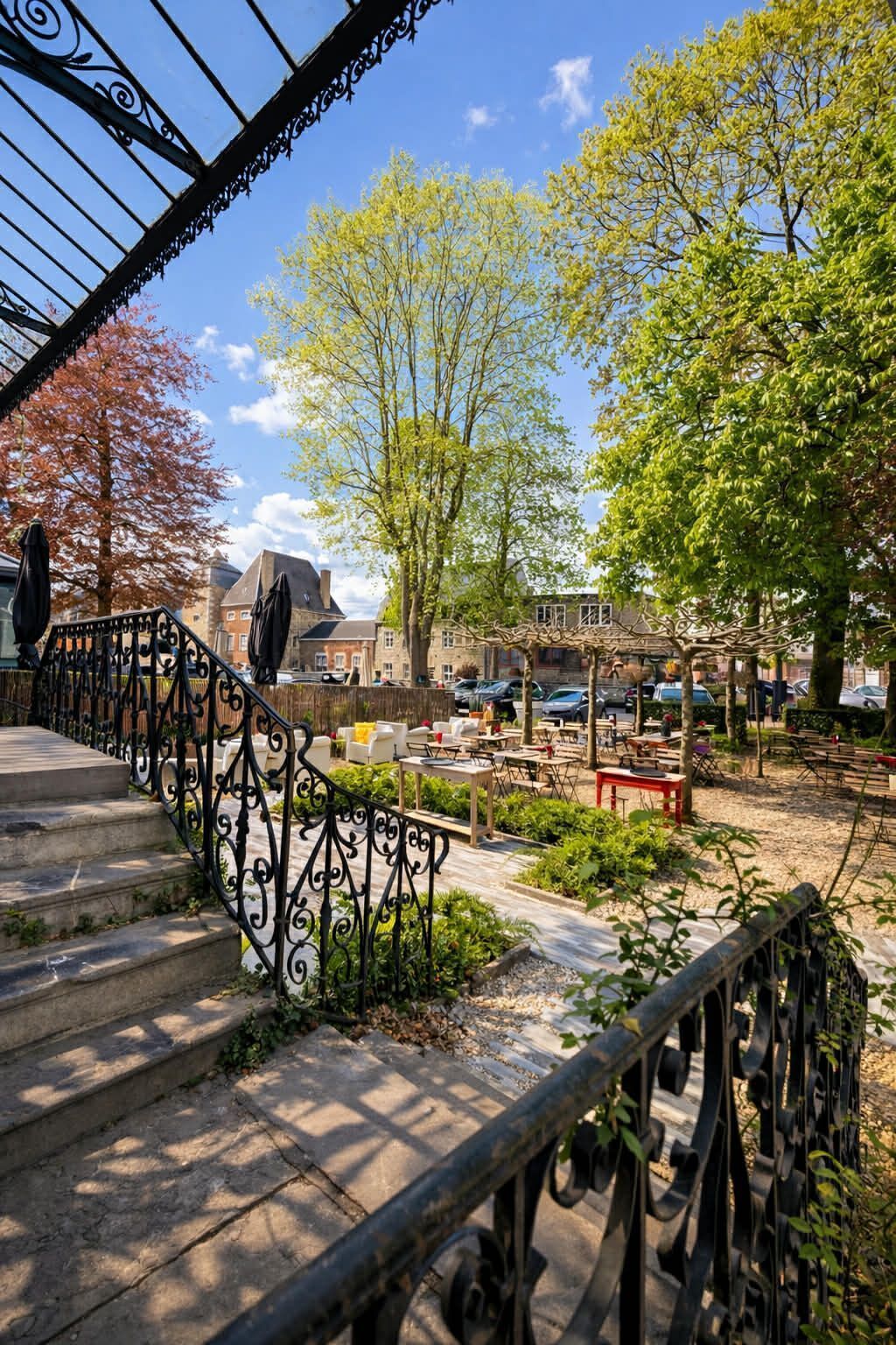 A courtyard with outdoor seating, a staircase with ornate railings, and a parking area in the background.