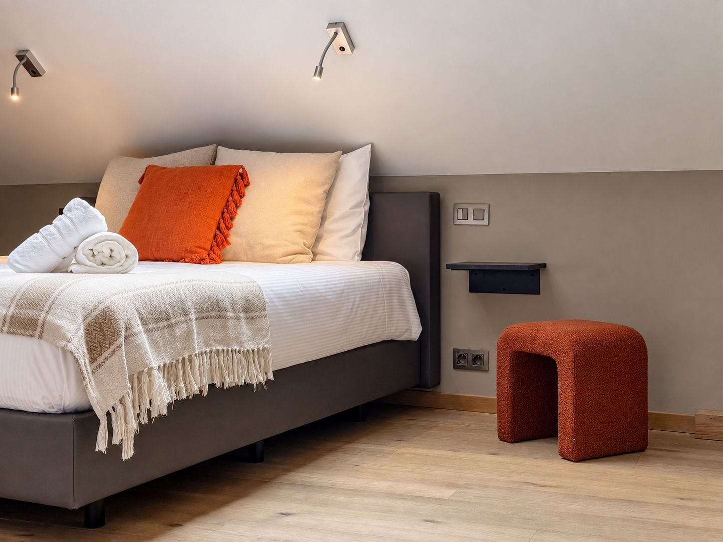 A modern bedroom with a bed, bedside tables, and a small stool.