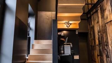 A modern staircase with wooden steps and a metal railing, leading to a room with a wooden wall and a coffee machine.