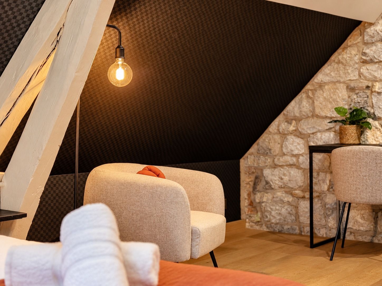 Una habitación acogedora con pared de piedra, suelo de madera, un sillón redondo, una mesita y una lámpara colgante.